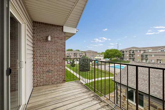 A balcony with a black railing and a brick wall with a pool view.