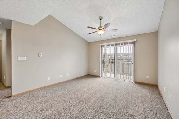 A spacious room with a ceiling fan and a sliding glass door leading to a balcony.