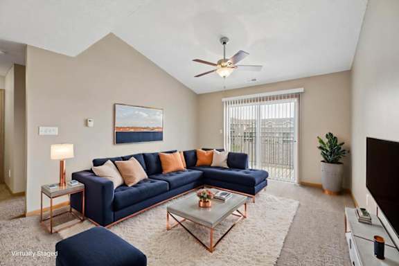 Virtually staged living room with a sectional sofa, coffee table, ceiling fan, large window, and neutral apartment finishes.