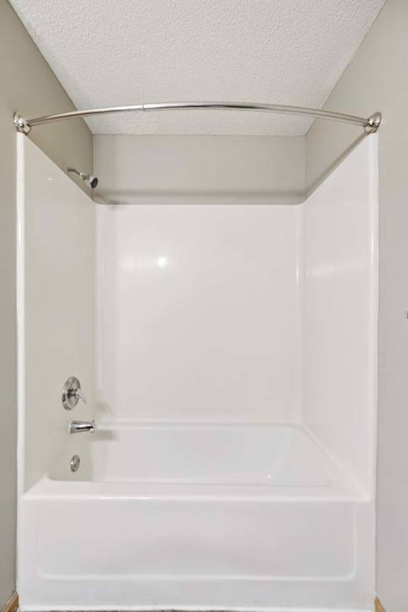 Apartment bathroom with a tub-shower combination featuring a white surround, built-in soap shelf, and curved shower curtain rod.