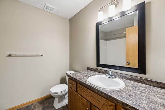 Apartment bathroom with a single-sink vanity, wood cabinetry, a granite-look countertop, a framed mirror with overhead lighting, and neutral wall finishes.