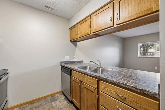 Apartment kitchen with wood cabinetry, black appliances, a double-basin sink, laminate countertops, and a pass-through opening connecting to the living area.