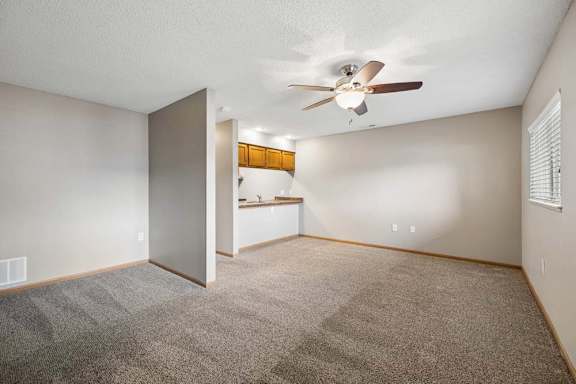 Spacious apartment living room with carpeted flooring, a ceiling fan, a pass-through to the kitchen, and a window with blinds providing natural light.