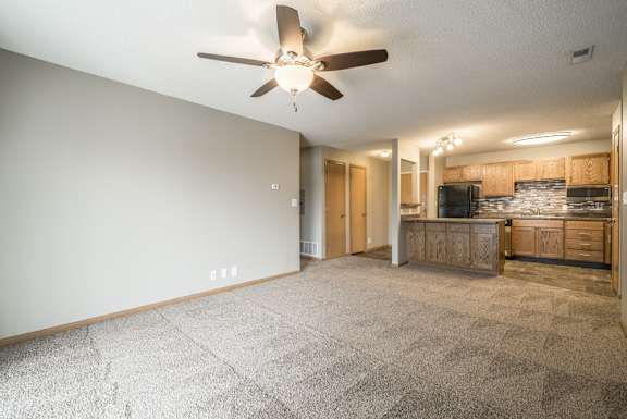 a spacious living room with a ceiling fan and a kitchen area in the background