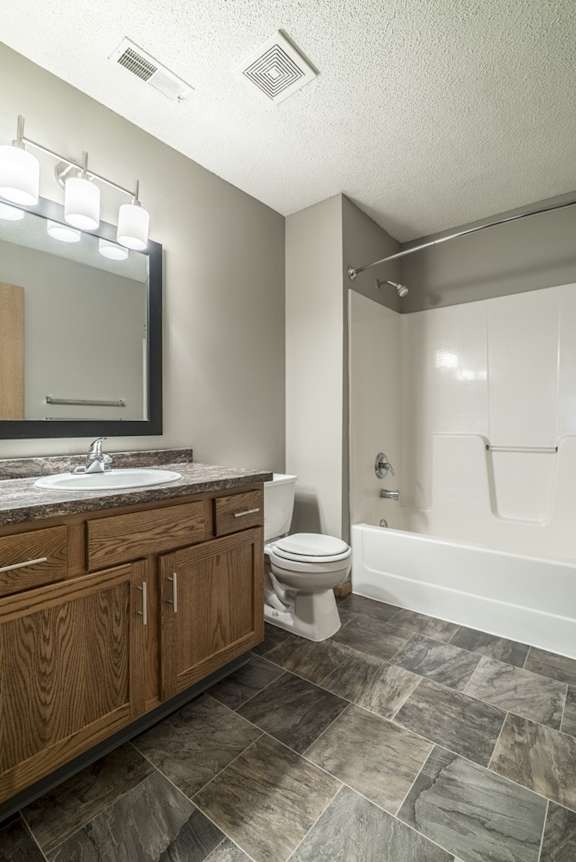 a bathroom with wooden cabinets, a granite vanity sink, a mirror, and a combination shower and tub
