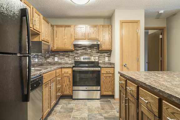 an updated kitchen featuring wooden cabinets, granite countertops, a tile backsplash, stainless steel appliances, and a kitchen island