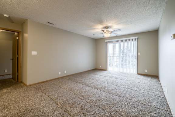 a carpeted living room with a ceiling fan and a sliding glass door to a balcony