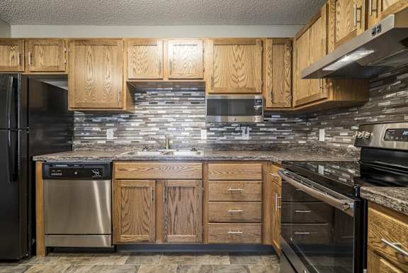 a kitchen with wooden cabinets, a tile backsplash, granite countertops, and stainless steel appliances