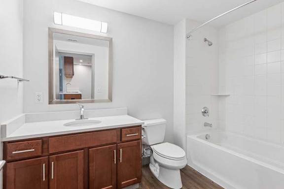 A bathroom with a granite vanity sink, a frame mirror with overhead lighting, and a tub shower.