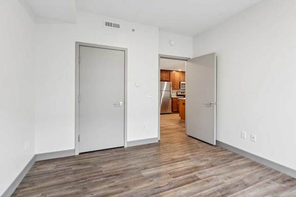 A bedroom with hardwood-style flooring, a closet walk-in closet, and a door open to the living room.