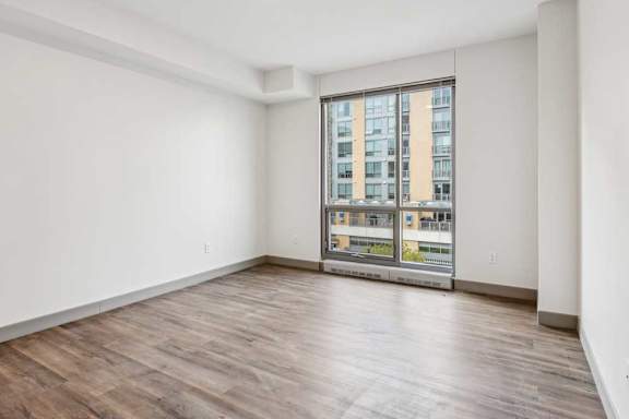 A bedroom with hardwood-style flooring, and a floor-to-ceiling window.