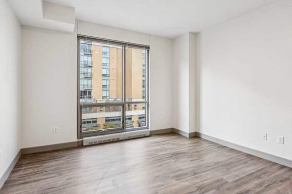 A bedroom with hardwood-style flooring, and a floor-to-ceiling window.