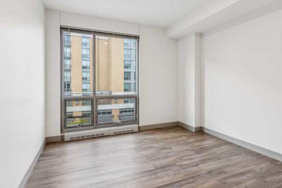 A bedroom with hardwood-style flooring, and a floor-to-ceiling window.