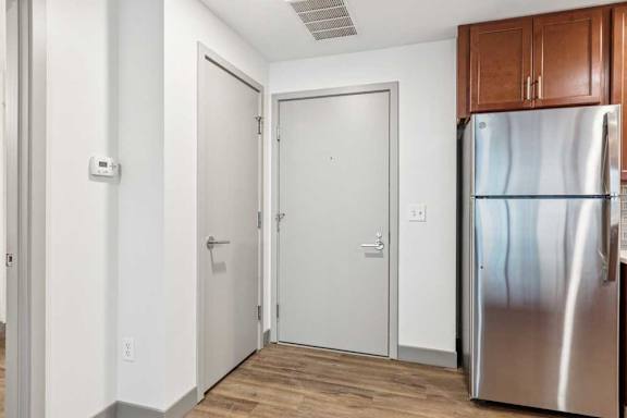 A front door next to a coat closet and a kitchen with a stainless steel fridge.