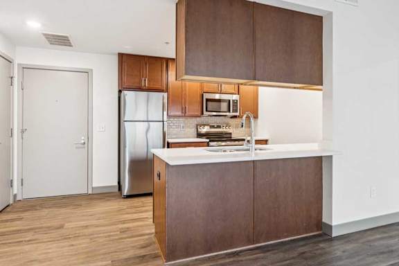 A modern kitchen with wooden cabinets, granite countertops, a tile backsplash, stainless steel appliances, and a peninsula with overhead cabinets.