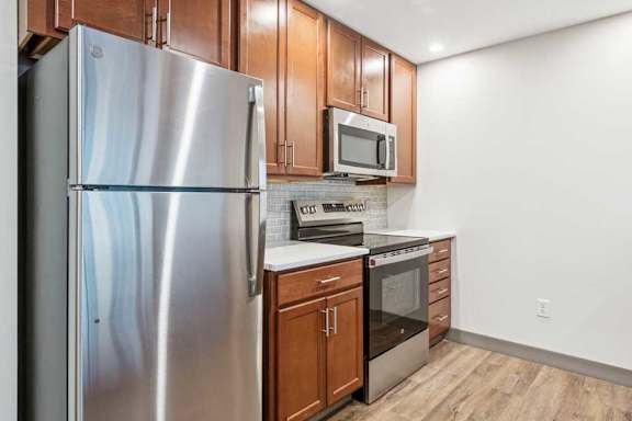 A modern kitchen with wooden cabinets, granite countertops, a tile backsplash, and stainless steel appliances.