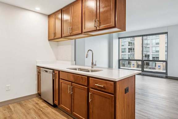 A kitchen peninsula with overhead wooden cabinets, granite countertops, and stainless steel appliances, in front of a living room.