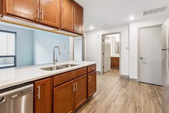 A kitchen peninsula with overhead wooden cabinets, granite countertops, and stainless steel appliances, in front of a living room.