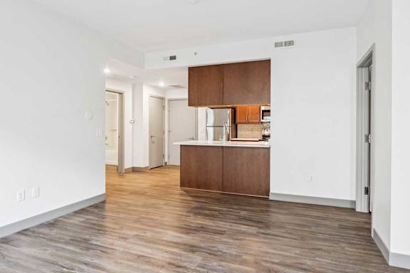 A living room with hardwood-style flooring the opens to a modern kitchen.