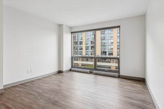 A living room with hardwood-style flooring and a large floor-to-ceiling window.