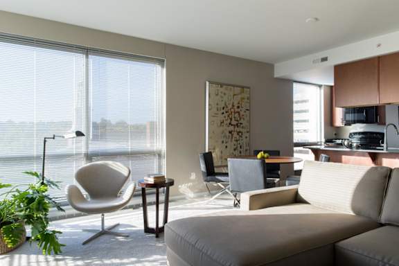 A living room with a grey sofa, a chair, a table, and huge windows