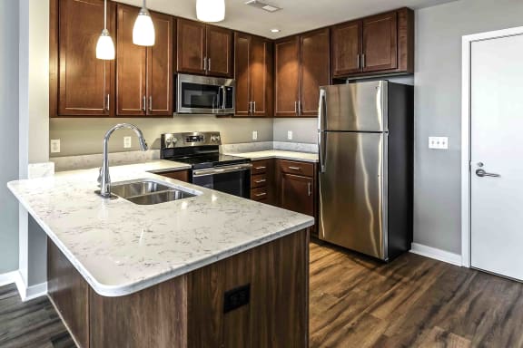 Full view of the kitchen with dark wood flooring and cabinets, stainless steel appliances and white quartz countertops in a one bedroom apartment at Midtown Crossing apartments