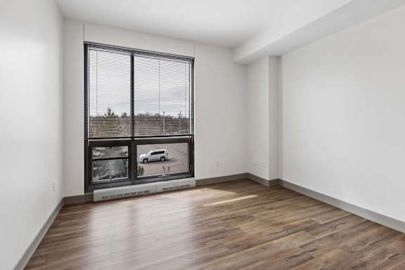 An empty apartment living room with vinyl wood flooring, a large floor to ceiling window, and a city view.