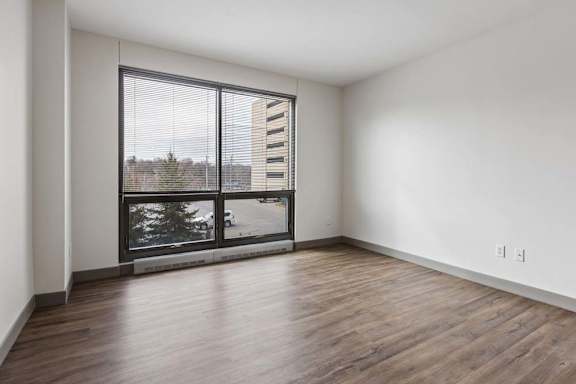 An empty apartment living room with vinyl wood flooring, a large floor to ceiling window, and a city view,.