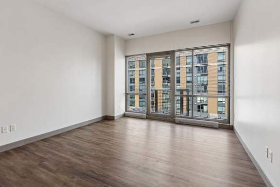 A room with wooden floors and a view of a building through the windows.