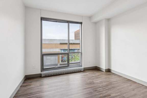 A bedroom with hardwood-style flooring, and a floor-to-ceiling window.