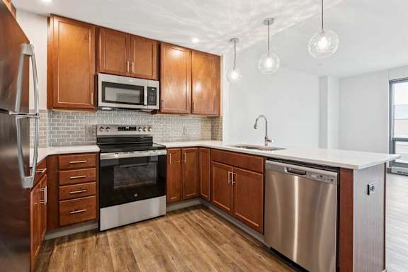 A modern kitchen with wooden cabinets, granite countertops, a tile backsplash, and stainless steel appliances.
