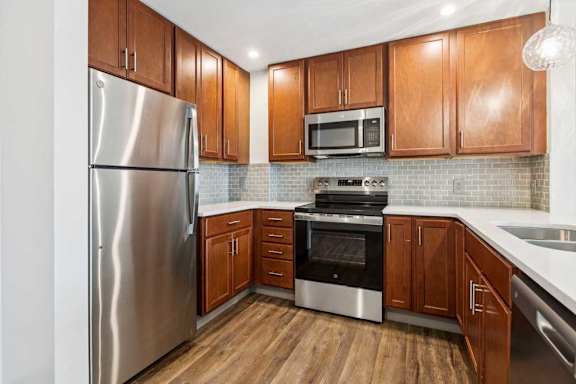 A modern kitchen with wooden cabinets, granite countertops, a tile backsplash, and stainless steel appliances.