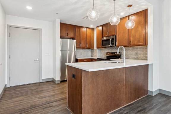 A modern kitchen with wooden cabinets, granite countertops, a tile backsplash, and stainless steel appliances.