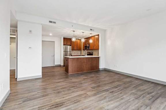A living room with hardwood-style flooring the opens to a modern kitchen.