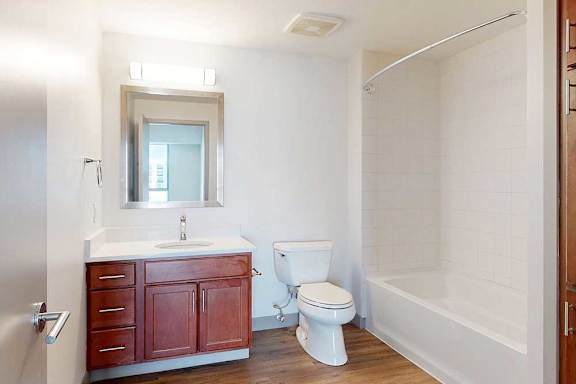A bathroom with a granite vanity, warm wooden cabinets, and a tub shower.