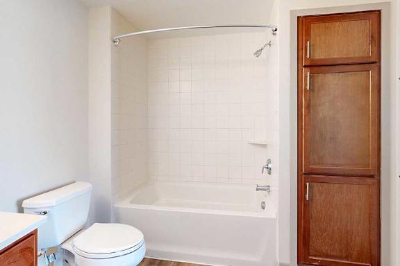 A bathroom with a wooden linen closet next to a tub shower.