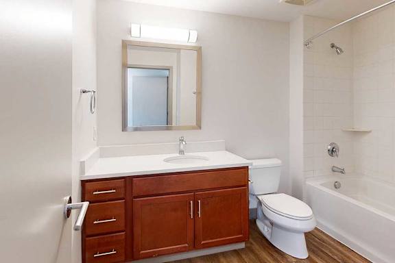 A bathroom with a granite vanity, warm wooden cabinets, and a tub shower.