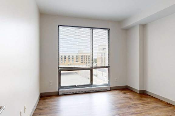 A bedroom with hardwood-style flooring and a floor-to-ceiling window.