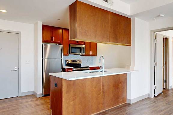 A kitchen with a peninsula with warm wooden cabinets and a white granite countertop.