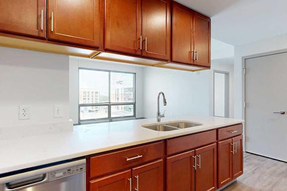 A kitchen with warm wooden cabinets, and a peninsula counter with sink overlooking a living room.