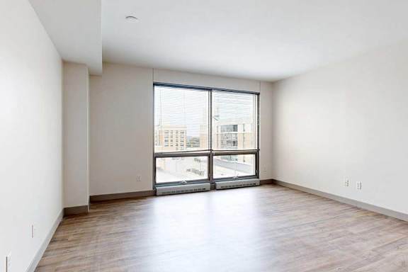 A living room with hardwood-style flooring and a floor-to-ceiling window.