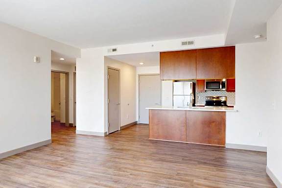 A living room with hardwood-style flooring and kitchen with warm wooden cabinets.