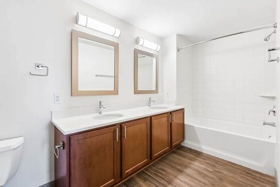A bathroom with a white tub, sink, and wooden cabinets.