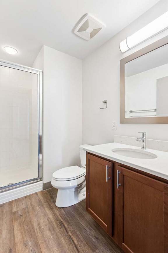 A white toilet sits in a bathroom with a wooden cabinet and a mirror above the sink.