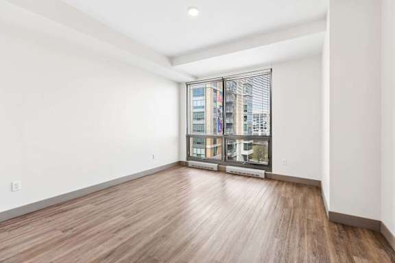 A room with wooden flooring and a large window with a view of a cityscape.