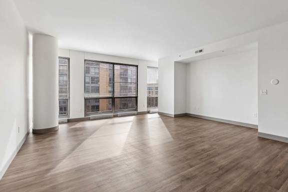 A spacious room with wooden flooring and large windows.