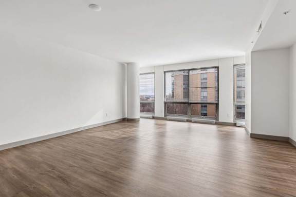 A large empty room with wooden floors and a view of a building outside the window.