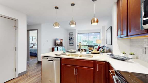 A kitchen with brown cabinets and a white countertop looking into living room