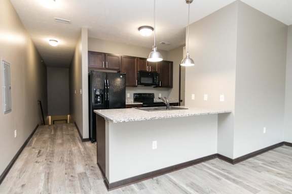 A kitchen with a black fridge and microwave, brown cabinets, and a white countertop.