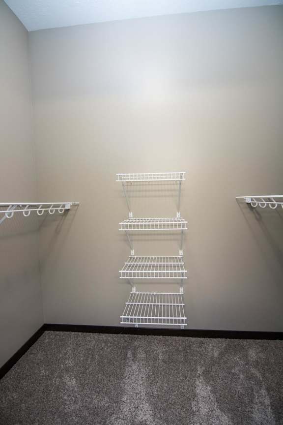 A walk-in closet with three white shelves on the wall.